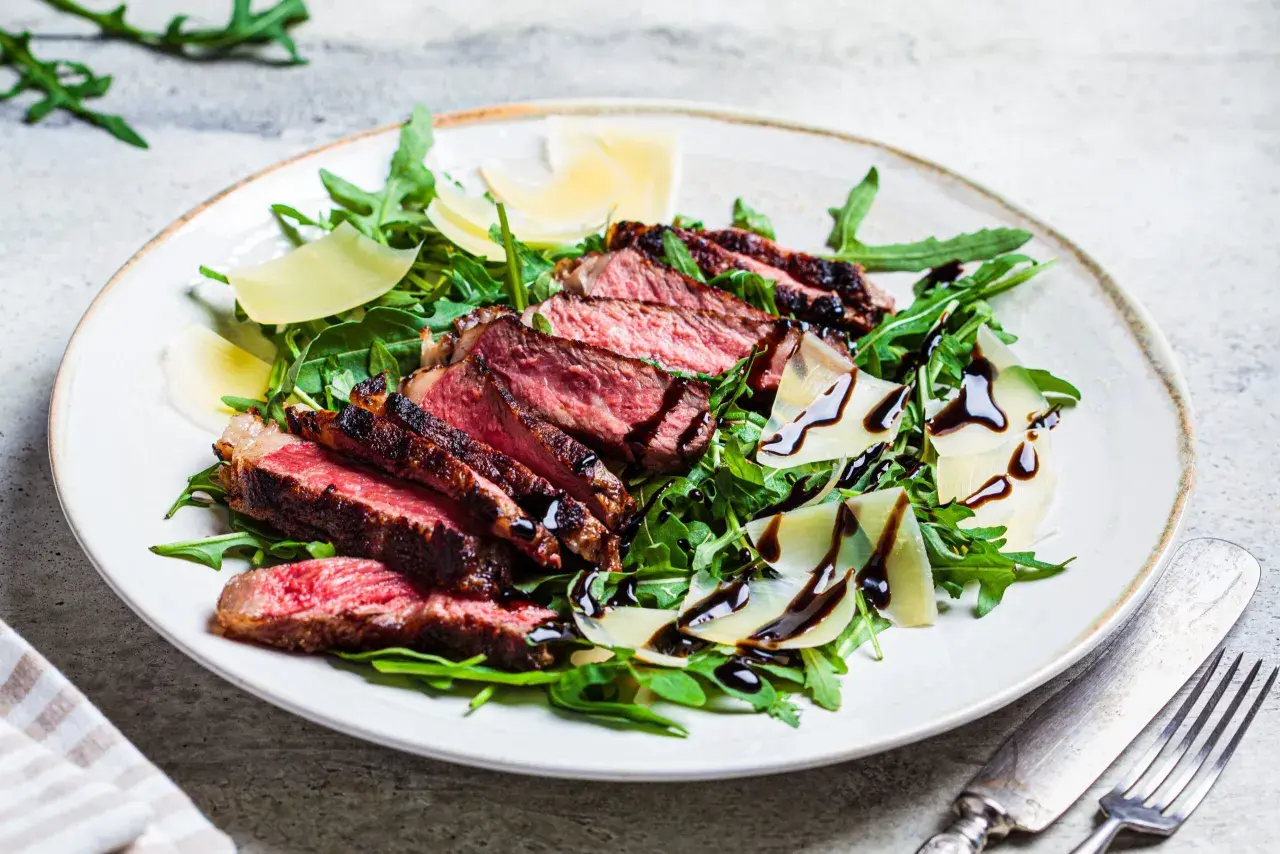 Une assiette de tagliata de boeuf, roquette, copeaux de parmesan et filet de vinaigre balsamique.