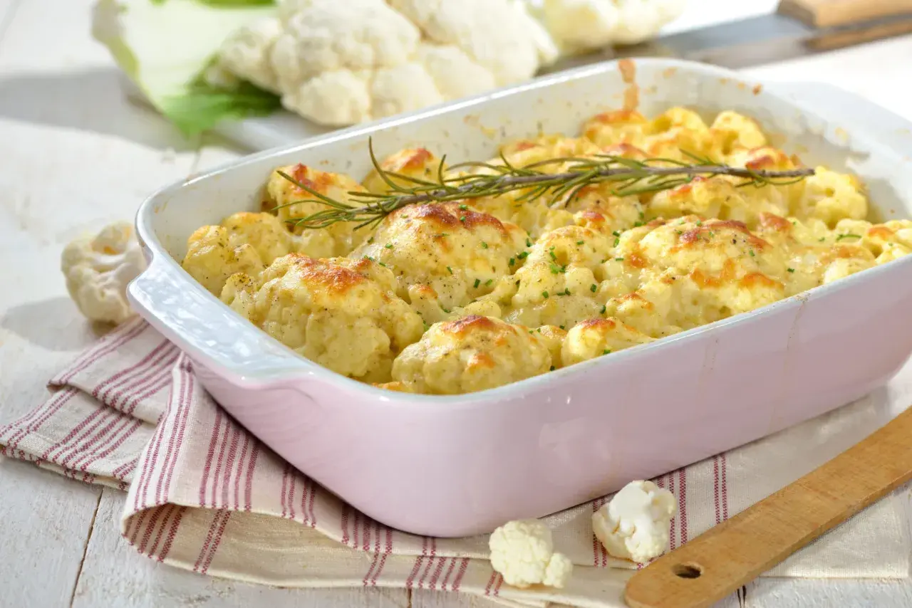 Un plat de gratin de chou-fleur doré et gratiné, garni de romarin frais, prêt à être dégusté.