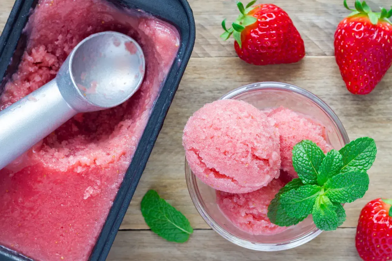 Un délicieux parfait glacé à la fraise, servi dans un bol avec des feuilles de menthe fraîche et des fraises entières.