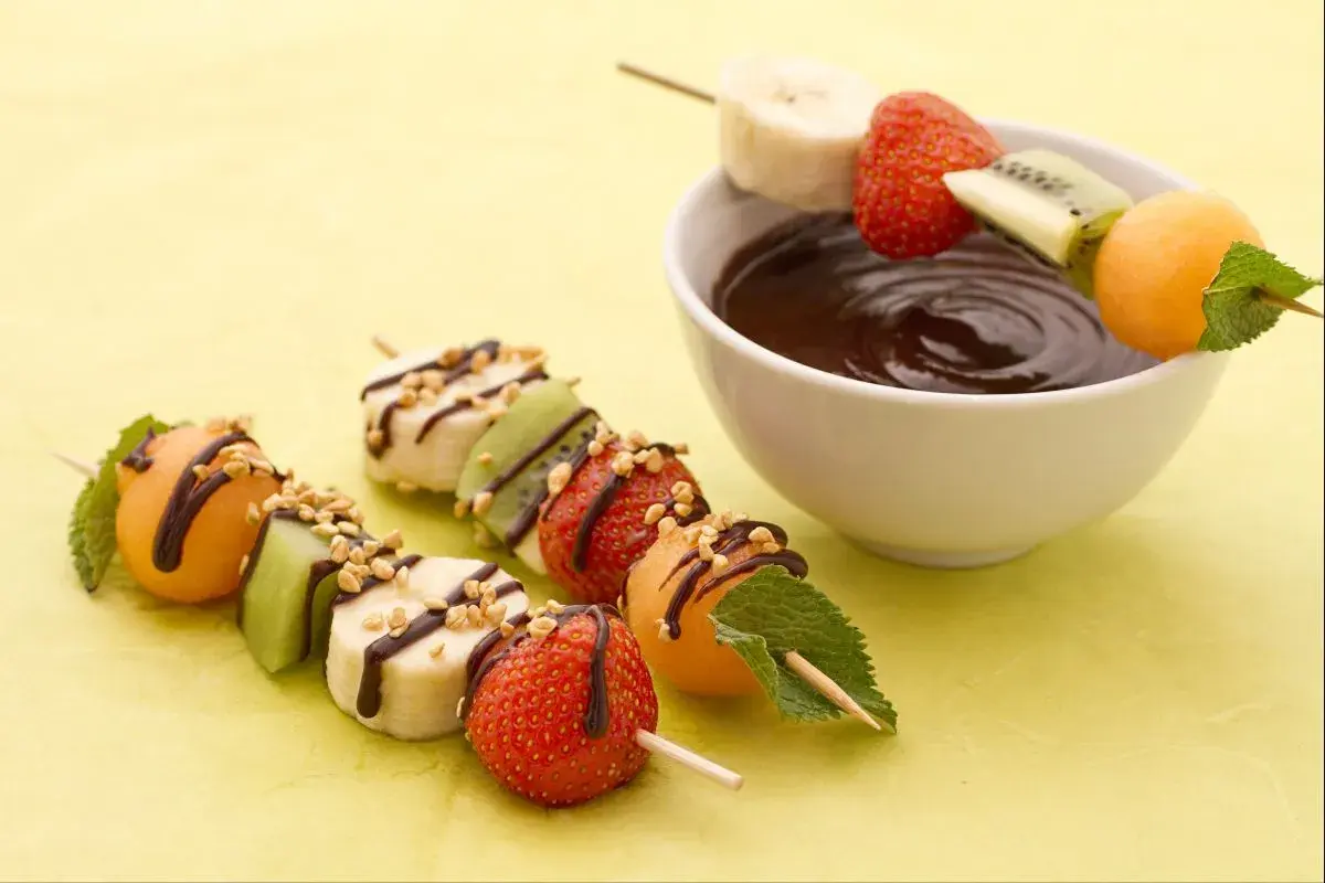 Délicieuses brochettes de fruits, bananes, fraises, kiwis et melons, arrosées de chocolat et de noix, prêtes à être trempées.