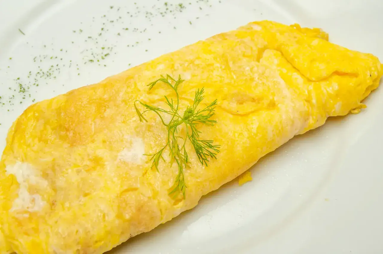 Une omelette au thon, dorée et moelleuse, garnie d'aneth frais sur une assiette blanche. Un délice simple et savoureux.