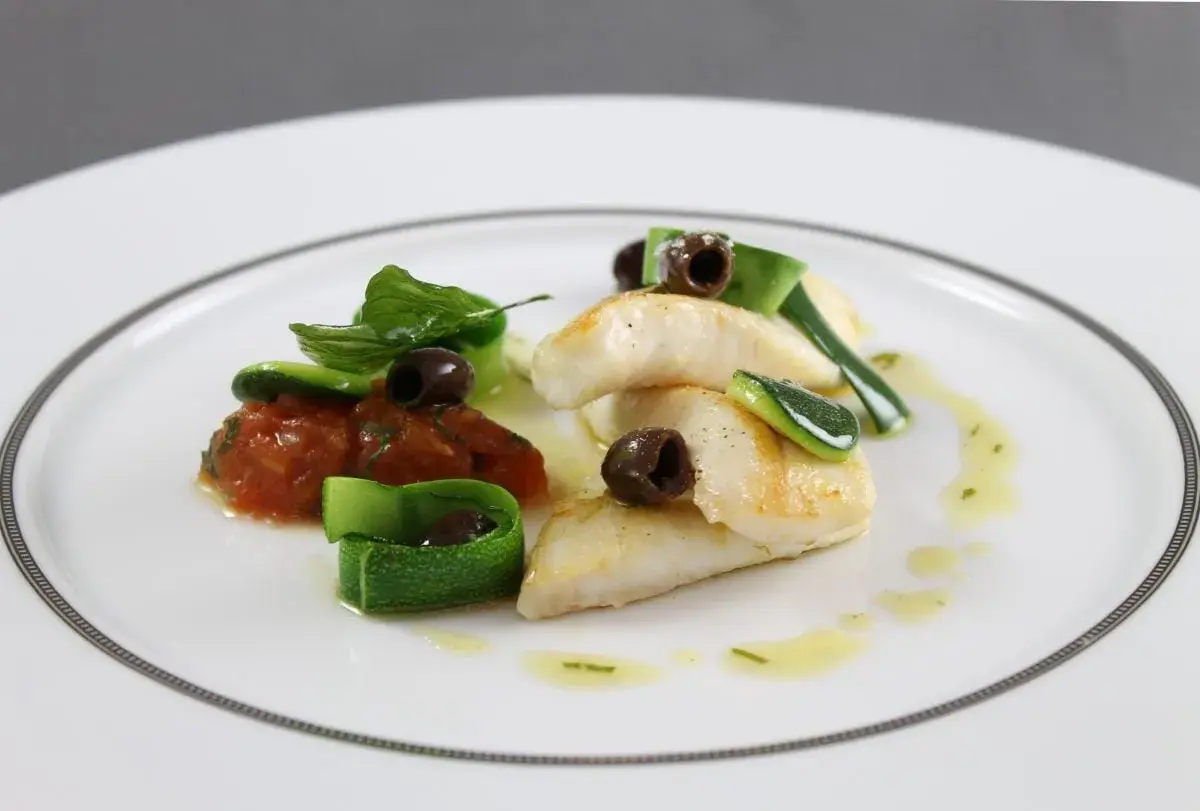 Délicieux filet de saint pierre poêlé, servi avec une concassée de tomates, des rubans de courgette et des olives noires.