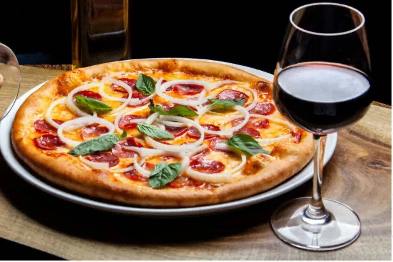 Une pizza garnie d'oignons et de pepperoni, accompagnée d'un verre de vin rouge. La question est : quel vin avec pizza ?