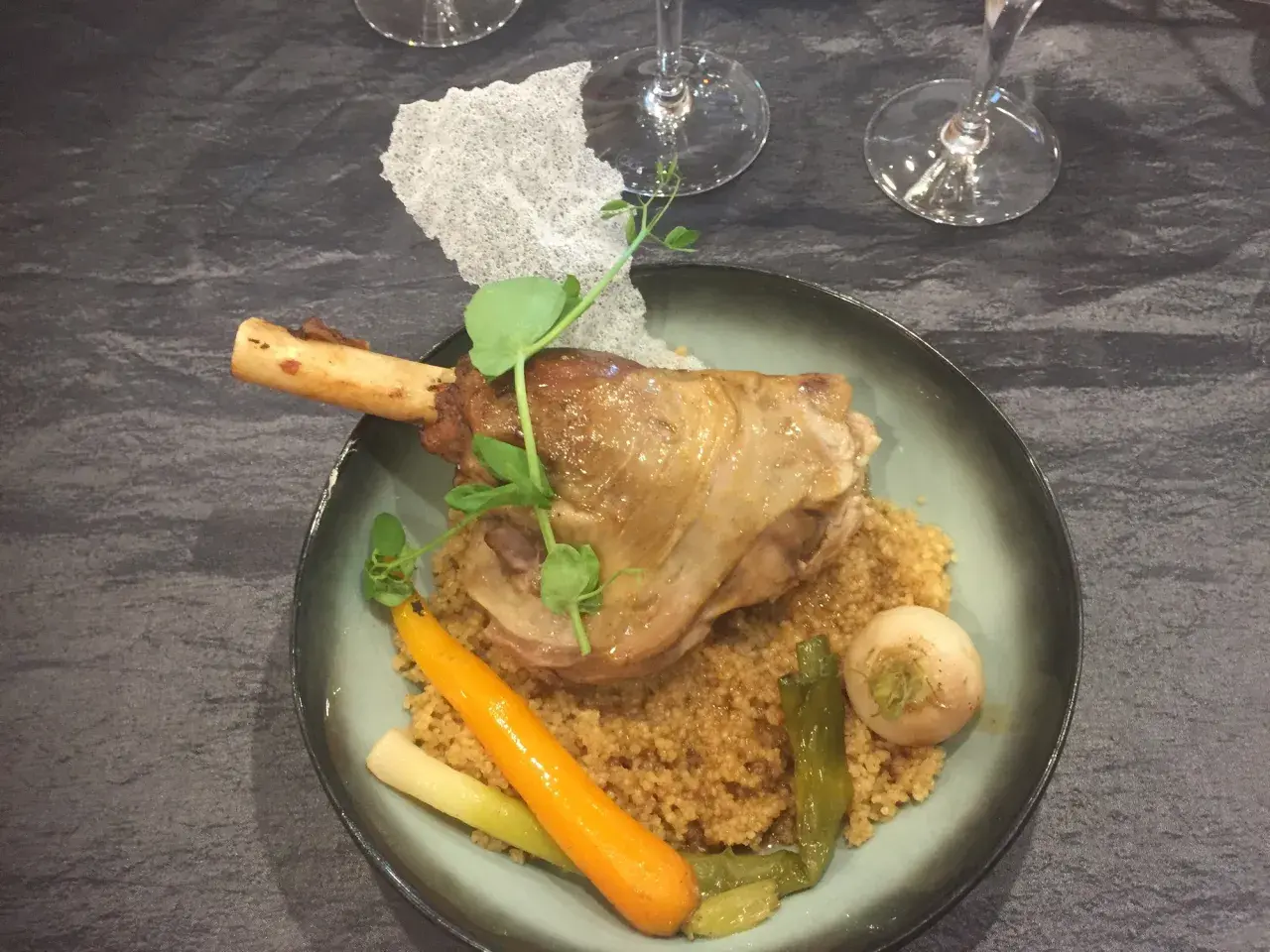 Souris d'agneau braisée au vin, servie sur un lit de couscous avec carottes et navets. Un plat savoureux et réconfortant.