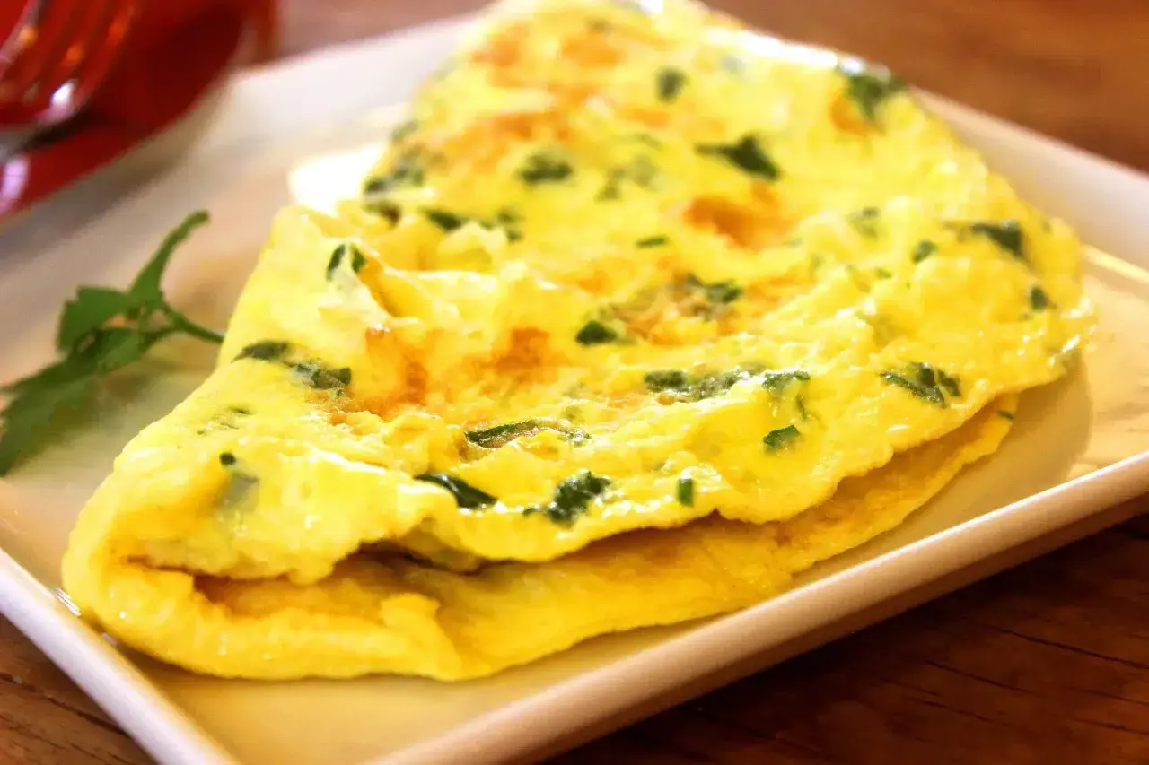 Une omelette au fromage, dorée et moelleuse, parsemée d'herbes fraîches, servie sur une assiette blanche.