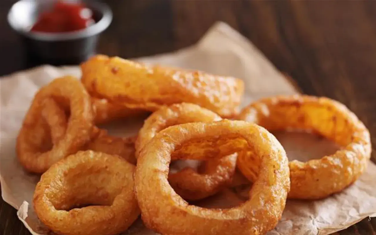 Un tas d'oignon rings dorés et croustillants, servis sur du papier brun, avec un petit bol de ketchup en arrière-plan.