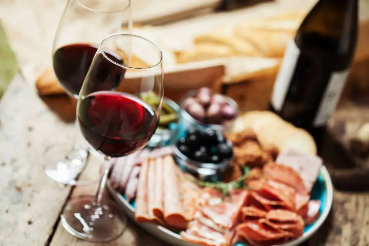Deux verres de vin rouge, une bouteille, une assiette de charcuterie variée, olives et cornichons. Parfait pour savoir quel vin avec charcuterie.