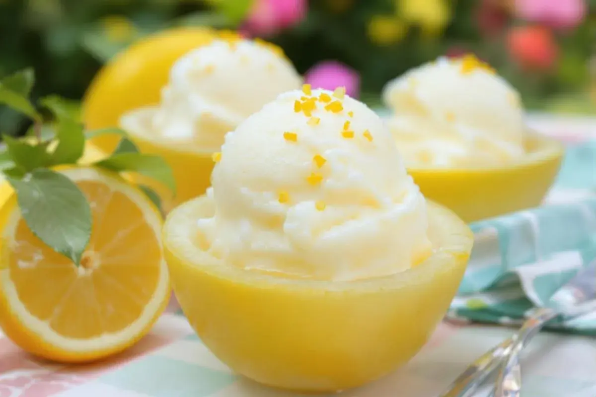 Trois coupes de citron givré, garnies de zestes d'orange, présentées dans des moitiés de citrons évidés. Un citron frais est visible à gauche.