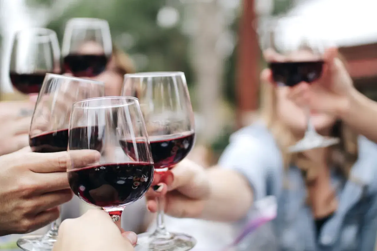 Des mains portent des verres remplis de vin rouge pour une dégustation conviviale en plein air.