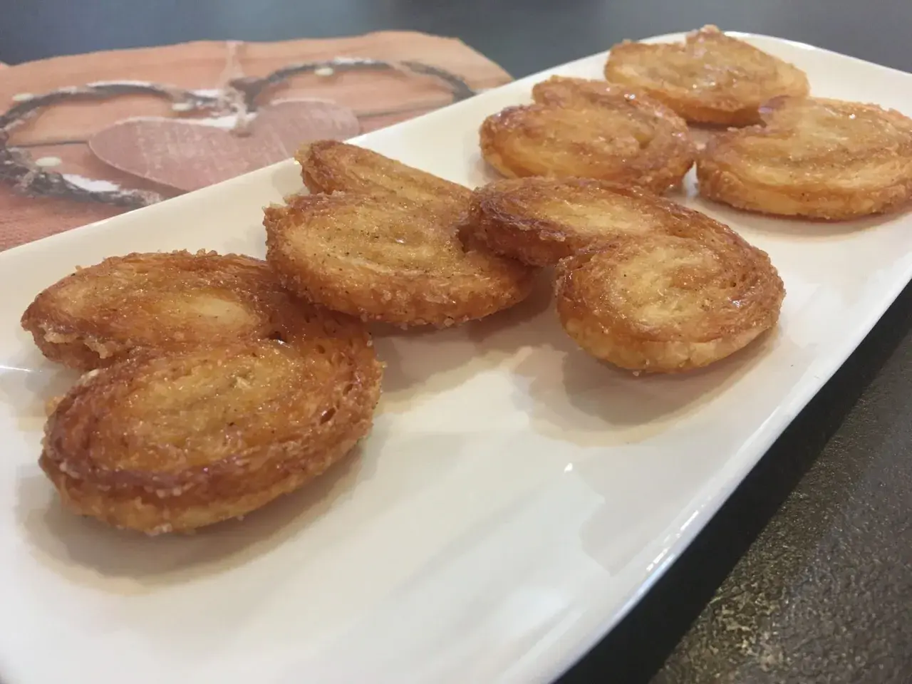 Une assiette blanche présente plusieurs palmiers croustillants, parfaits pour une recette facile.