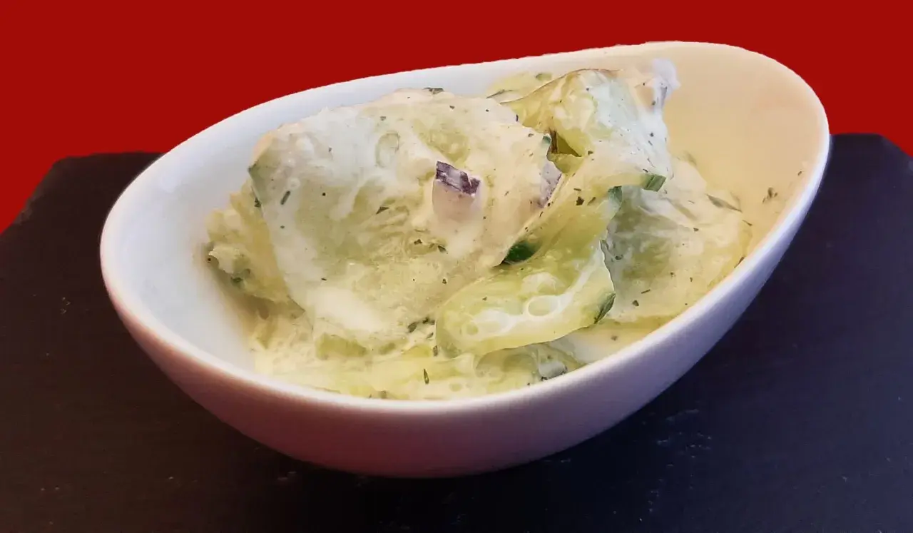 Un bol de concombre à la crème, garni d'herbes fraîches, prêt à être dégusté.
