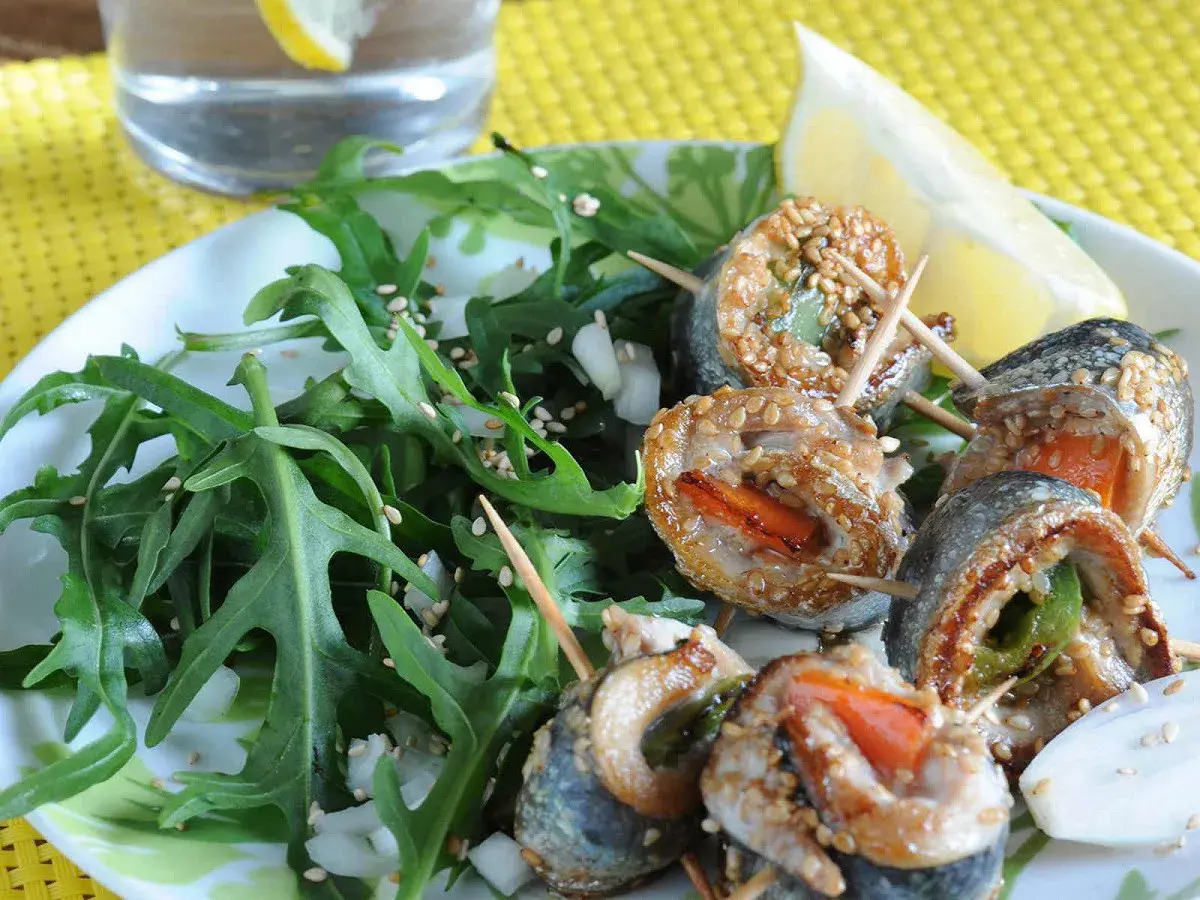 Rouleaux de sardines à la plancha, enrobés de sésame, servis avec une salade verte et un quartier de citron.