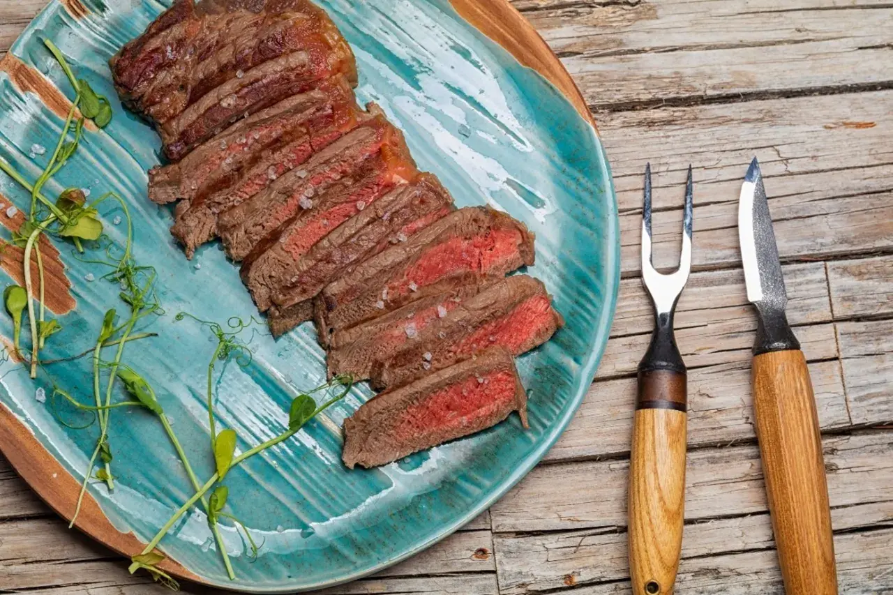 Tranches d'onglet de bœuf saignant, parsemées de gros sel, sur une assiette turquoise. Une recette simple pour un plat savoureux.