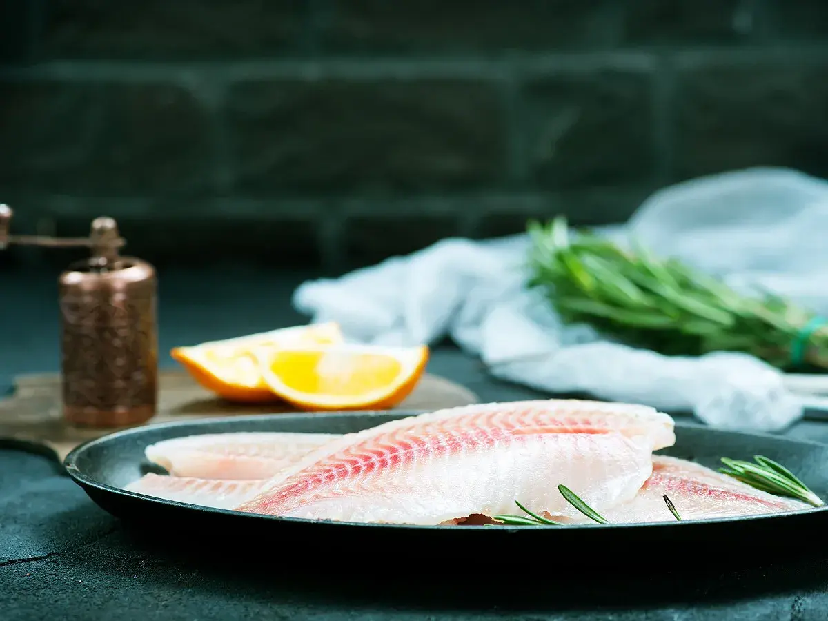 Filets de poisson crus dans une poêle, prêts pour un maquereau au vin blanc. Oranges et romarin à proximité.