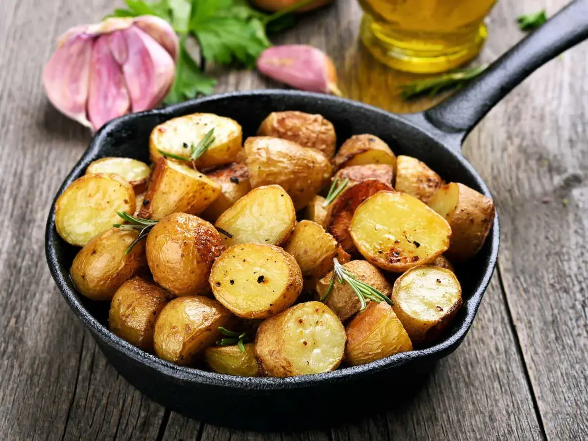 Poêlée de pommes de terre sautées dorées et croustillantes, garnies de romarin frais, avec de l'ail et de l'huile d'olive en arrière-plan.