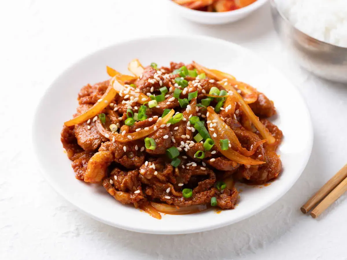 Délicieux boeuf aux oignons, garni de graines de sésame et de ciboule, servi sur une assiette blanche.
