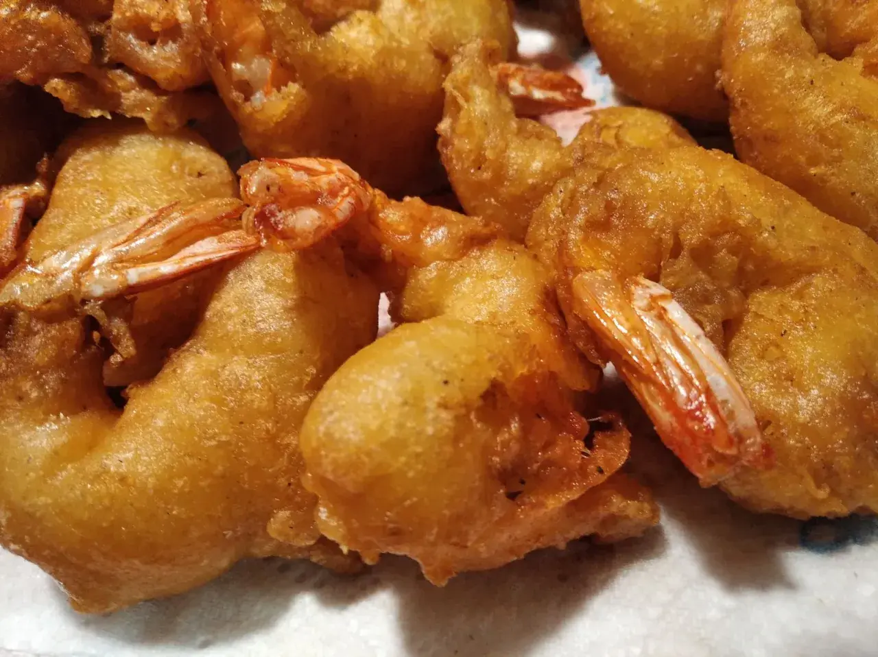 Gros plan sur des beignets de crevette dorés et croustillants, prêts à être dégustés. Les queues des crevettes dépassent de la pâte.