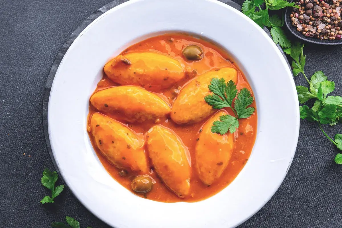 Assiette de quenelles de brochet en sauce tomate, garnie de persil et d'olives.