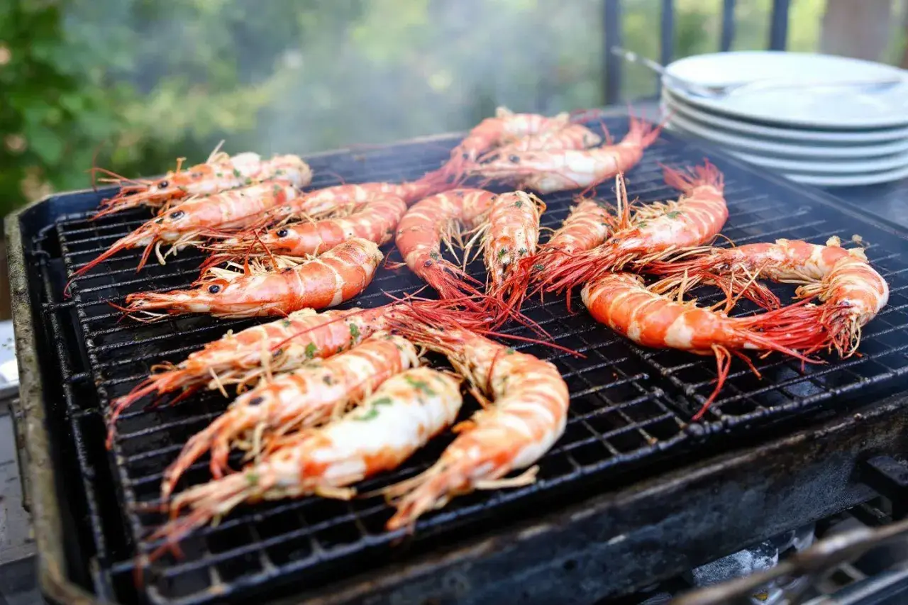 Grosses gambas barbecue sur un grill, fumant et appétissant. Les crevettes sont bien caramélisées, prêtes à être dégustées.