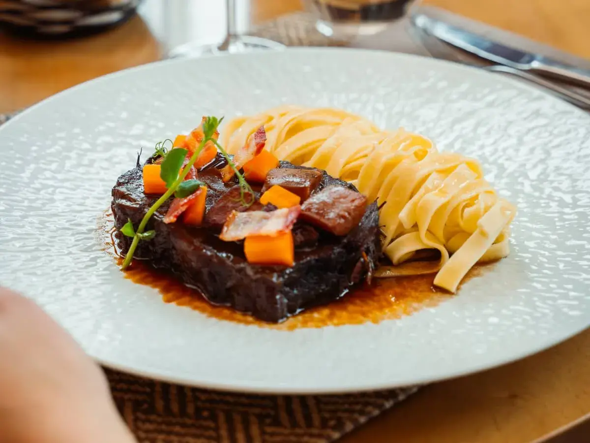 Un paleron de bœuf braisé, garni de dés de carottes et de lardons, servi avec des tagliatelles fraîches. Une recette savoureuse à découvrir.
