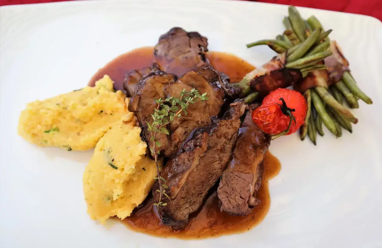 Savoureux sabodet au vin rouge, servi avec une polenta crémeuse, des haricots verts enroulés de lard et une tomate confite.