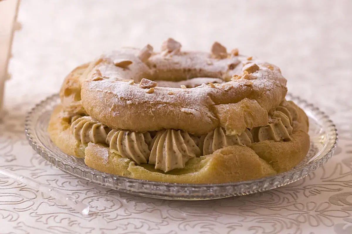 Un Paris-Brest garni d'une généreuse crème mousseline praliné, saupoudré de sucre glace et d'éclats de noisettes.