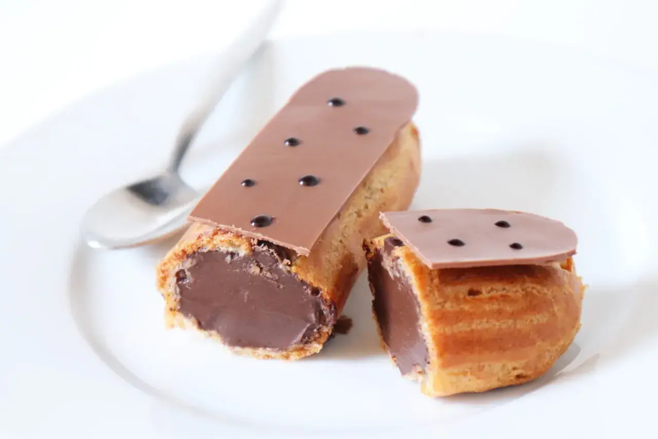 Deux éclairs au chocolat, un entier et un coupé, sur une assiette blanche avec une cuillère. Parfait pour une recette éclair au chocolat.