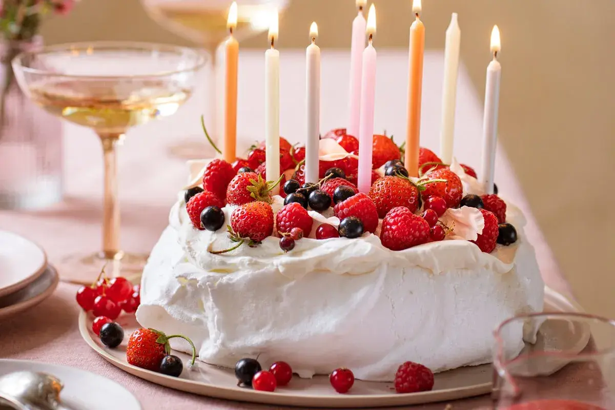 Pavlova fruit rouge, ornée de fraises, framboises et myrtilles, avec des bougies allumées pour une fête gourmande.