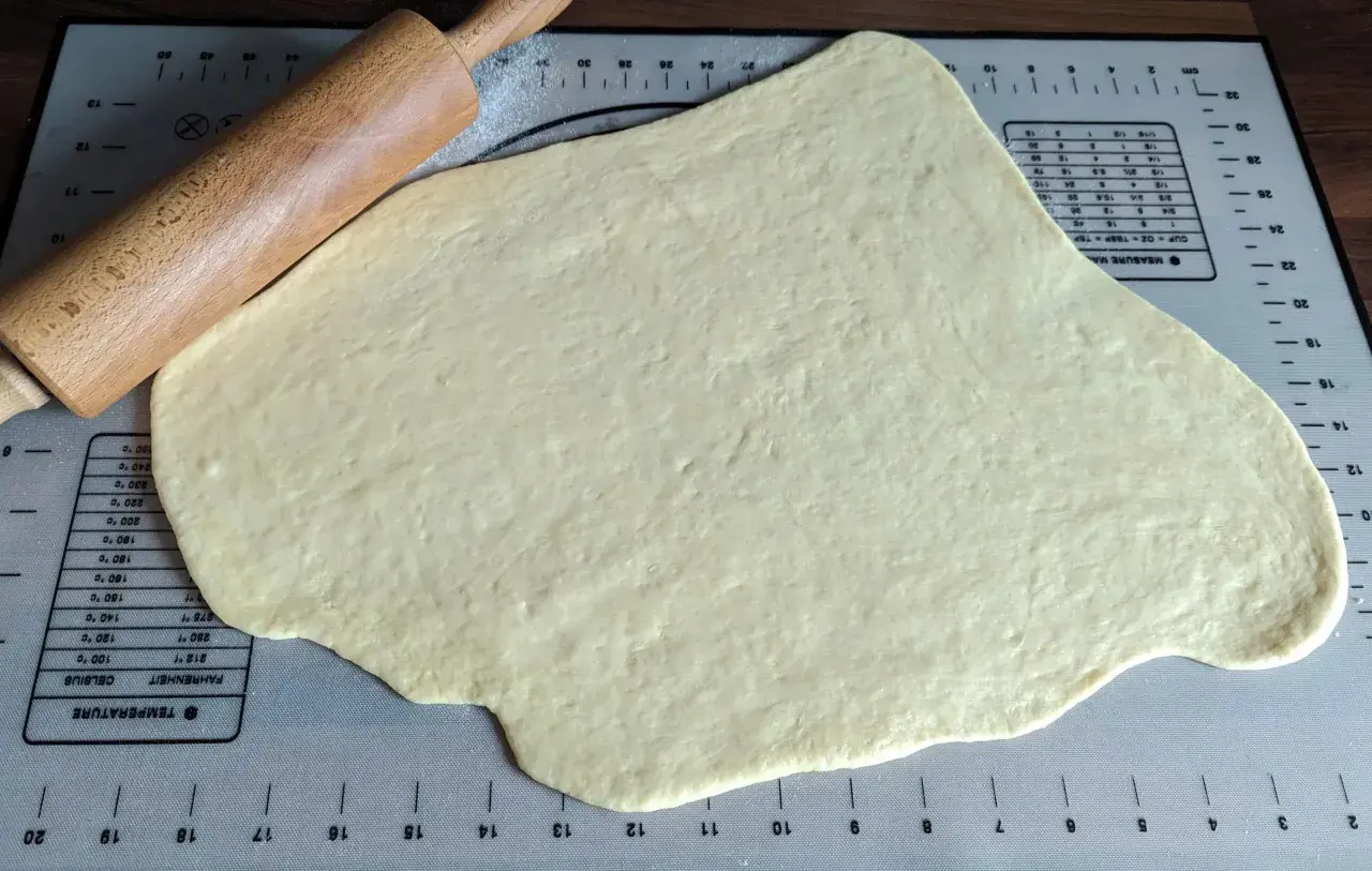 Pâte à beignet légère et croustillante étalée sur un tapis de pâtisserie avec un rouleau à pâtisserie.