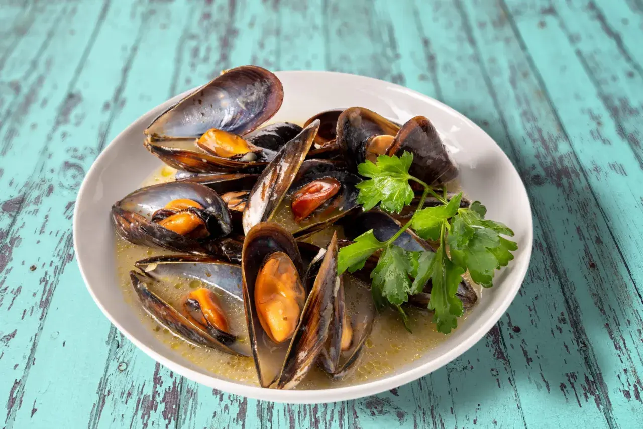 Un plat de moules au roquefort, garni de persil frais, baignant dans une sauce crémeuse. Un délice savoureux sur une table en bois bleu délavé.