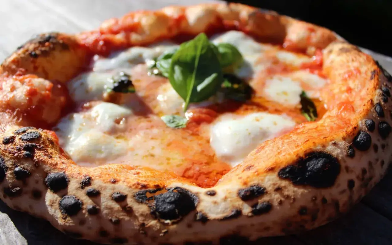 Une pizza napolitaine authentique, avec sa croûte gonflée et tachetée, garnie de sauce tomate, mozzarella fondante et basilic frais. La recette parfaite pour un délice italien.