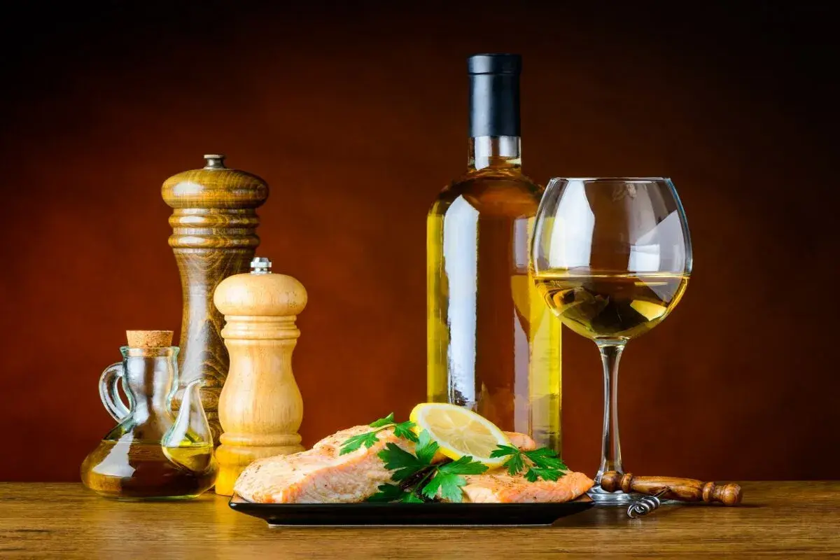 Un plat de saumon avec citron et persil, accompagné d'une bouteille et d'un verre de bon vin blanc sec, d'une salière, d'une poivrière et d'une burette d'huile d'olive.