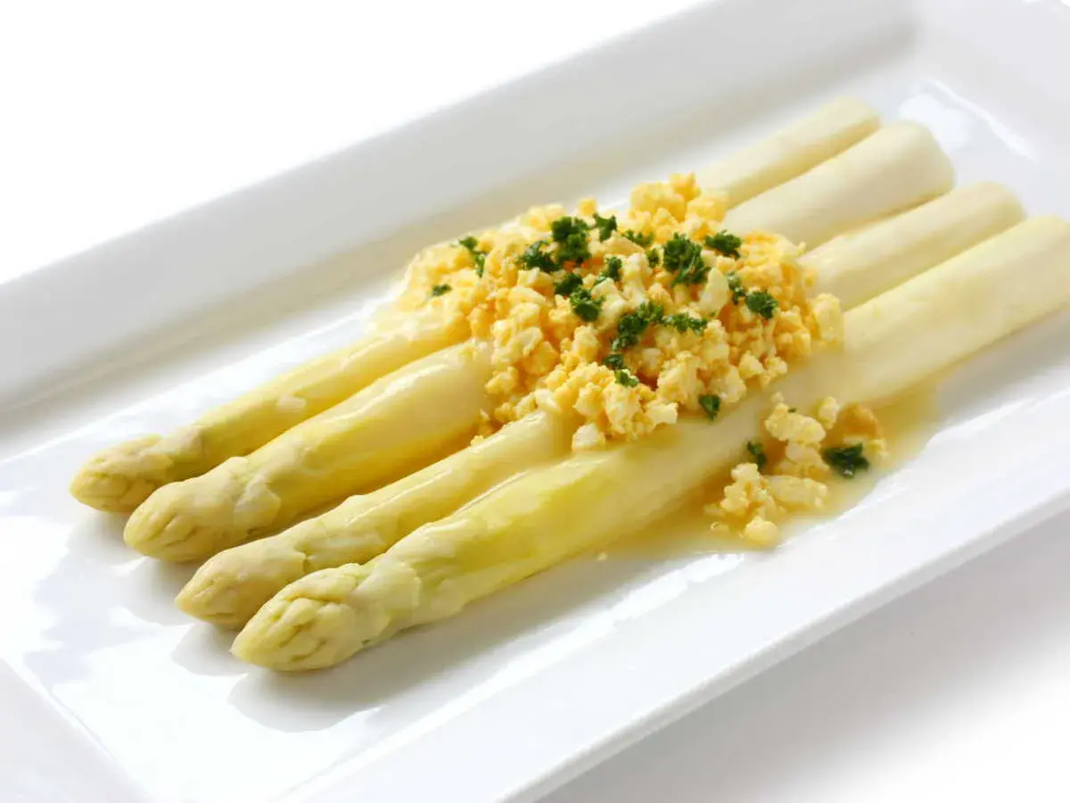 Asperges à la flamande : des asperges blanches tendres nappées d'une sauce savoureuse et garnies d'œufs brouillés et de persil frais.