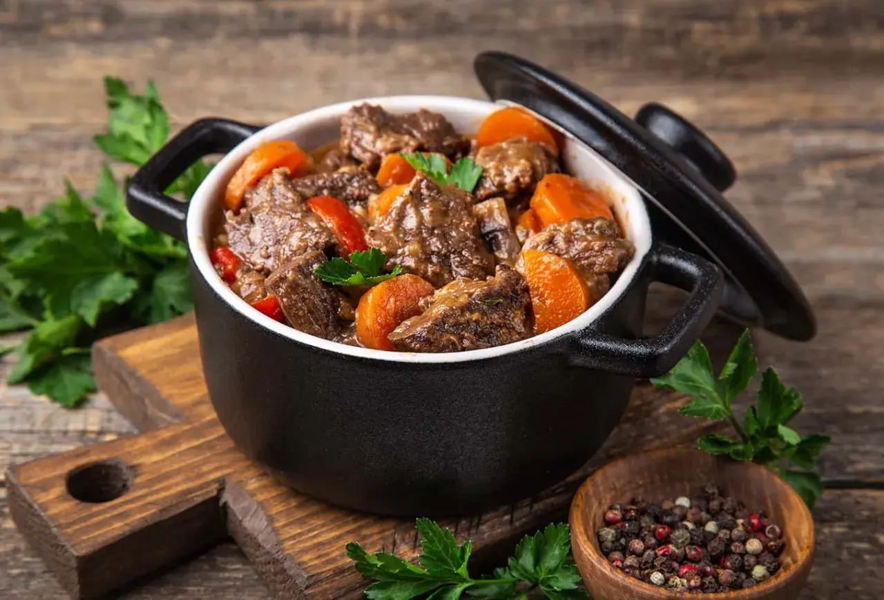 Un délicieux bœuf bourguignon mijoté dans une cocotte minute SEB, garni de carottes et de persil frais. Un plat réconfortant prêt à être dégusté.