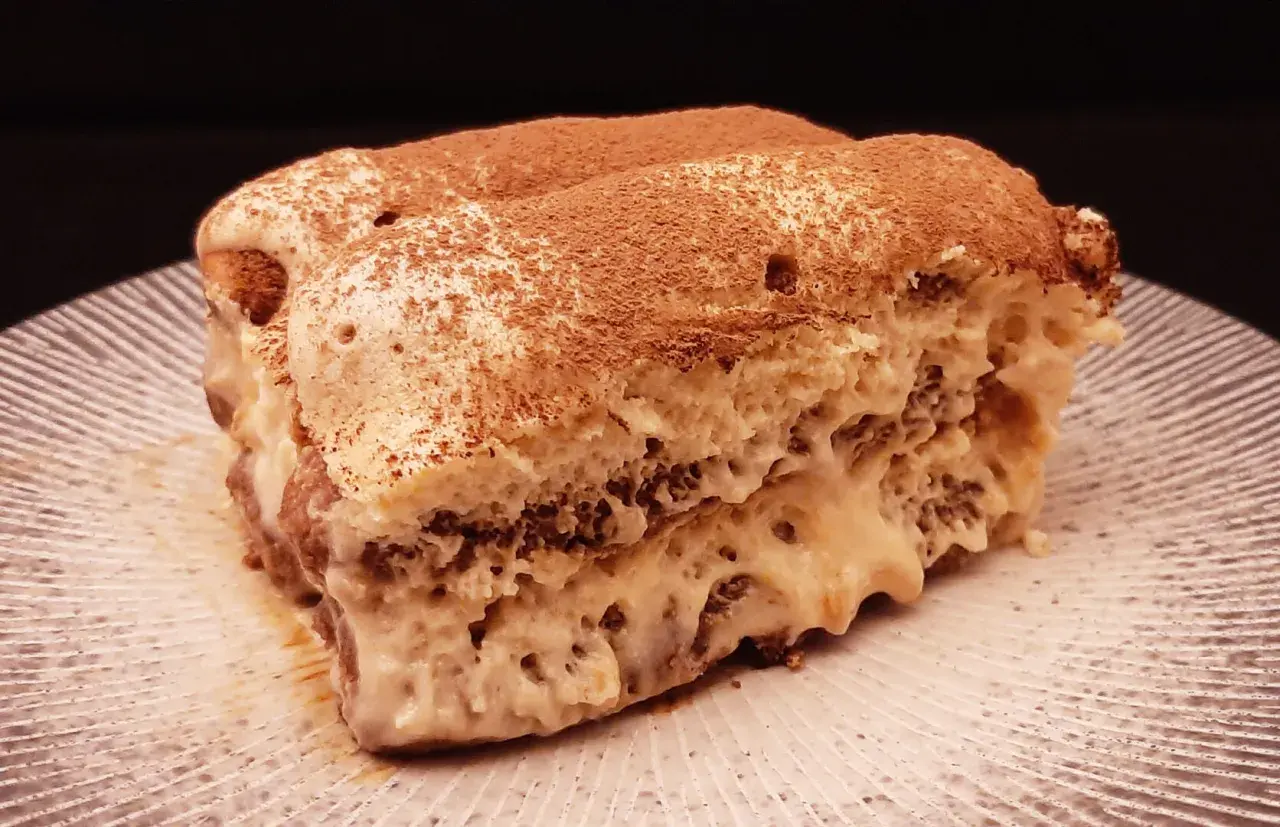Un généreux tiramisu au café, saupoudré de cacao, repose sur une assiette striée.