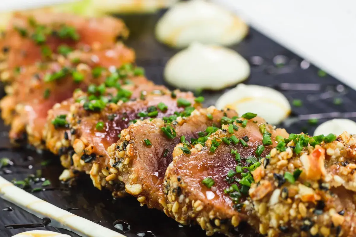 Tataki de thon en croûte de sésame et noix, garni de ciboule fraîche. Un accompagnement visuellement appétissant.
