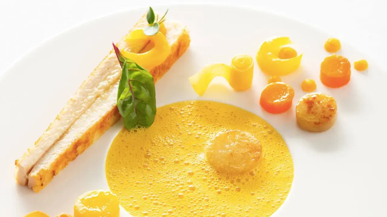 Une assiette élégante pour une recette d'omble chevalier : poisson poêlé, écume de carotte, et légumes croquants.