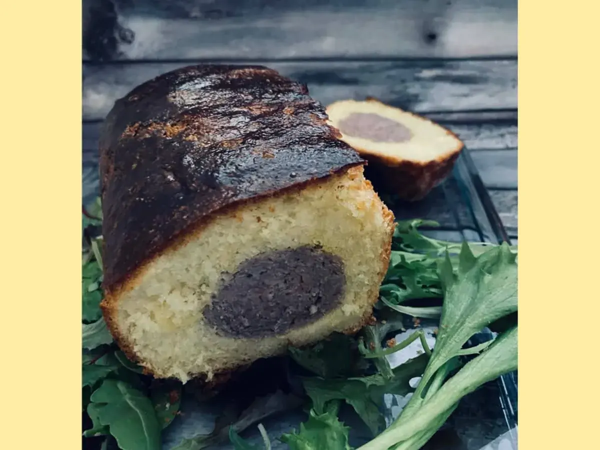 Un délicieux saucisson brioché, coupé en deux, repose sur un lit de verdure. Sa croûte dorée et sa mie moelleuse invitent à la dégustation.