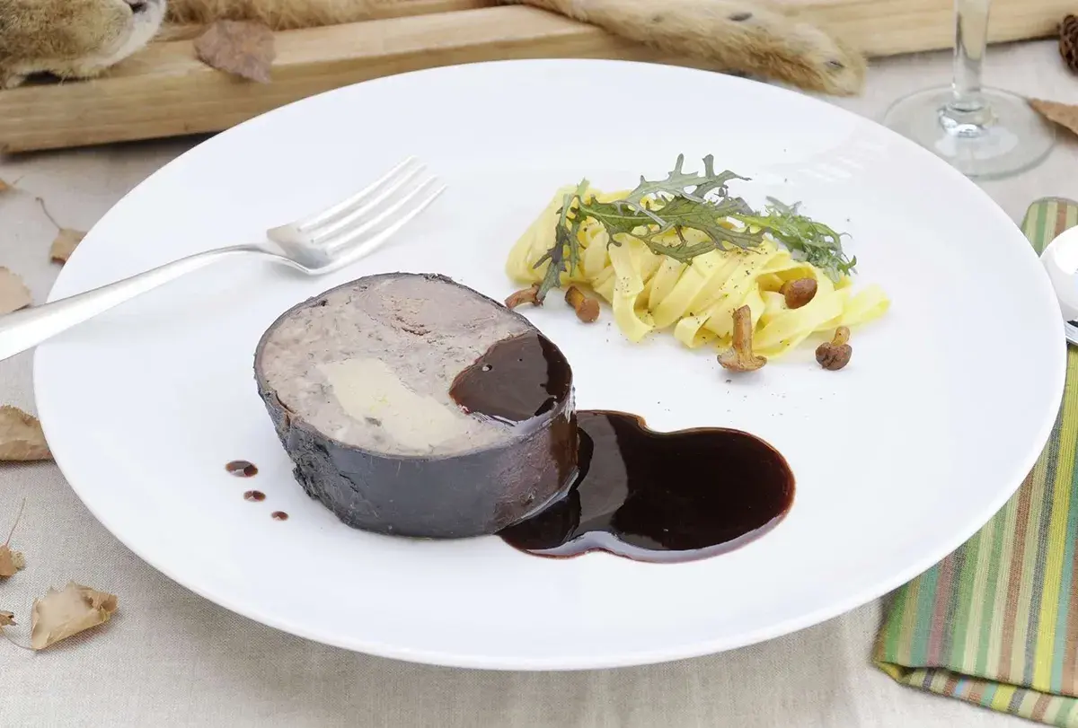 Un rôti de lièvre à la royale, garni de foie gras, servi avec des pâtes fraîches, des champignons et une sauce au vin.