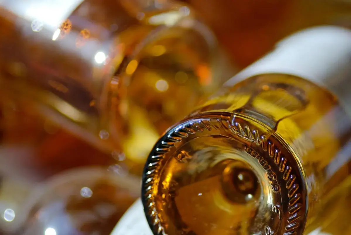 Gros plan sur le goulot d'une bouteille de vin ambré, évoquant un sauterne sec ou moelleux. Reflets lumineux sur le verre.