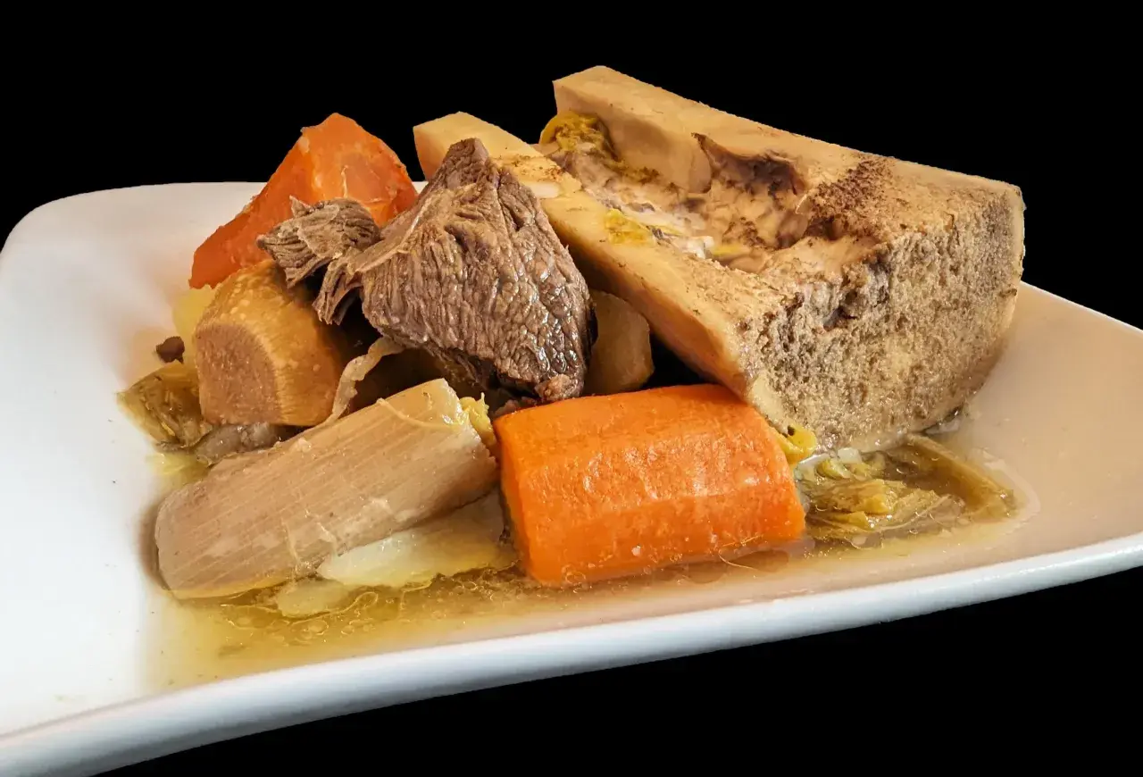 Un plat généreux de pot-au-feu cocotte minute : viande, os à moelle, carottes et poireaux mijotés dans un bouillon savoureux.