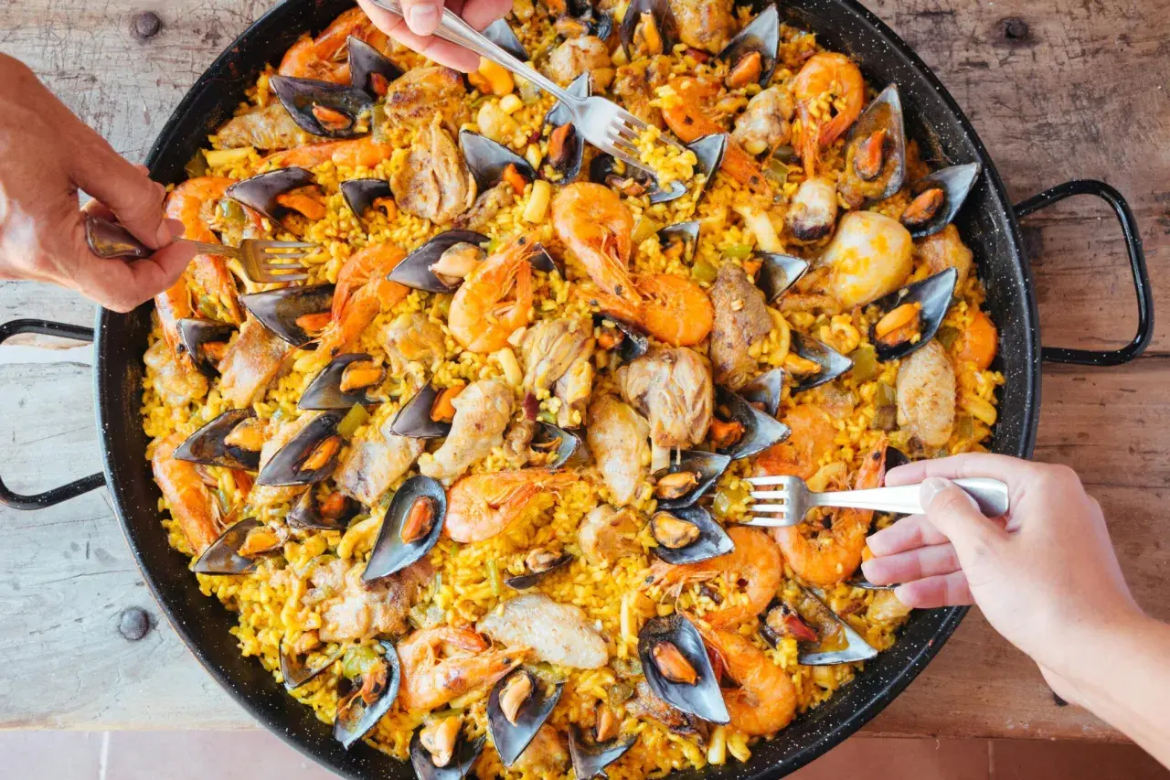 Un plat généreux de riz façon paella, garni de crevettes, moules et morceaux de poulet, prêt à être dégusté.