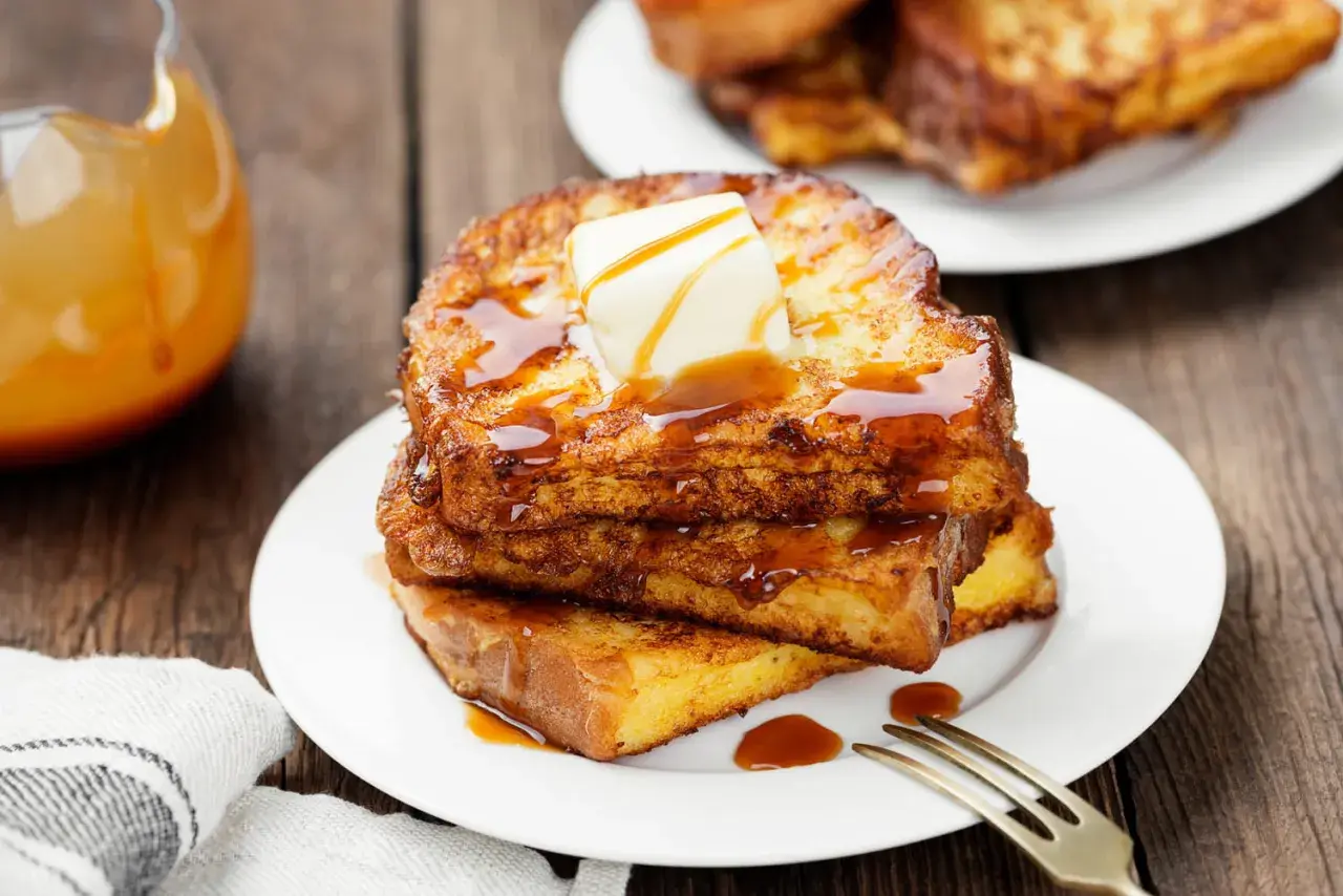 Pile de pain perdu doré, nappé de sirop et garni de beurre fondant. Un délice matinal.
