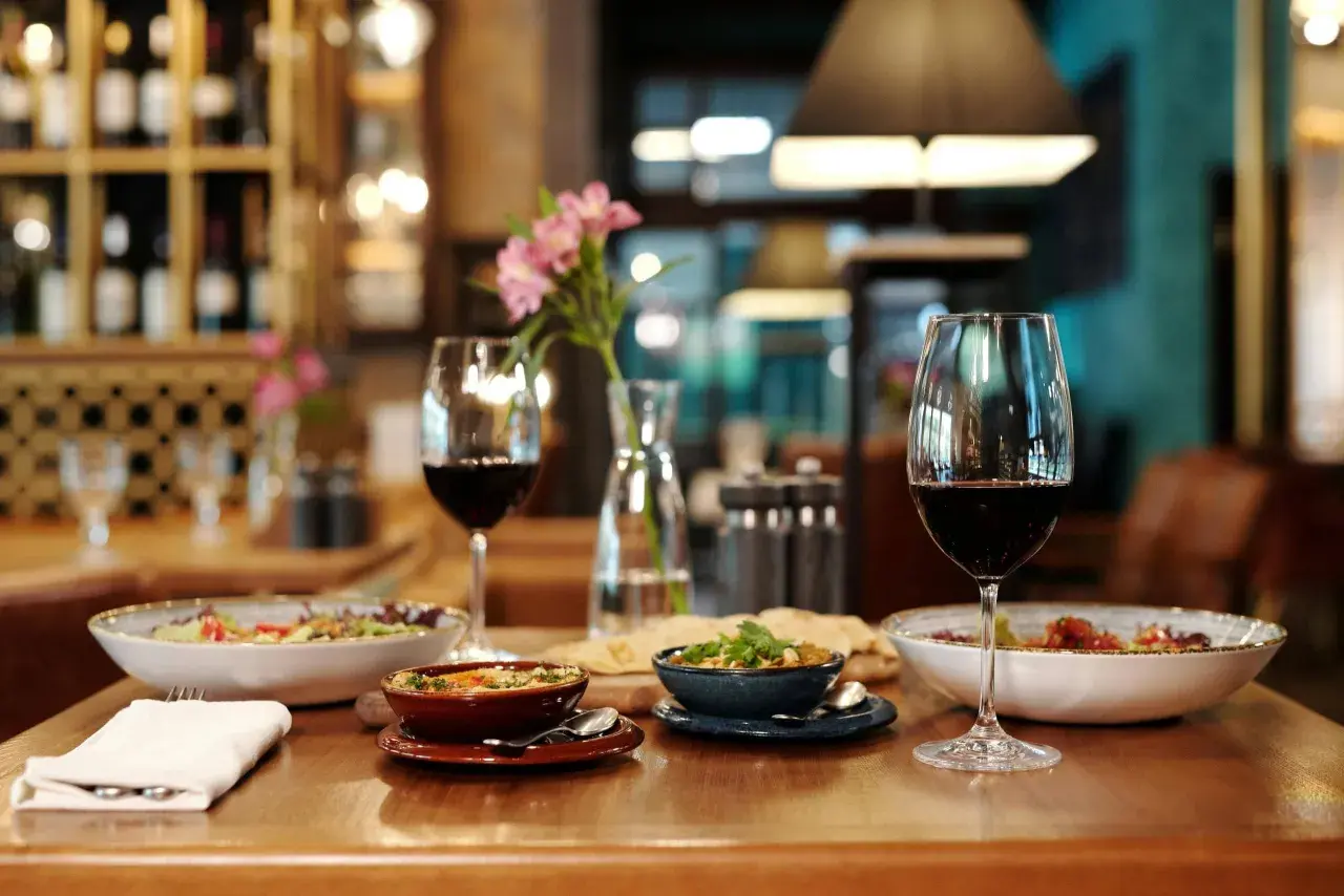 Verre de vin rouge tannique et puissant, accompagné de plats appétissants et d'une touche florale, dans une ambiance de restaurant chaleureuse.