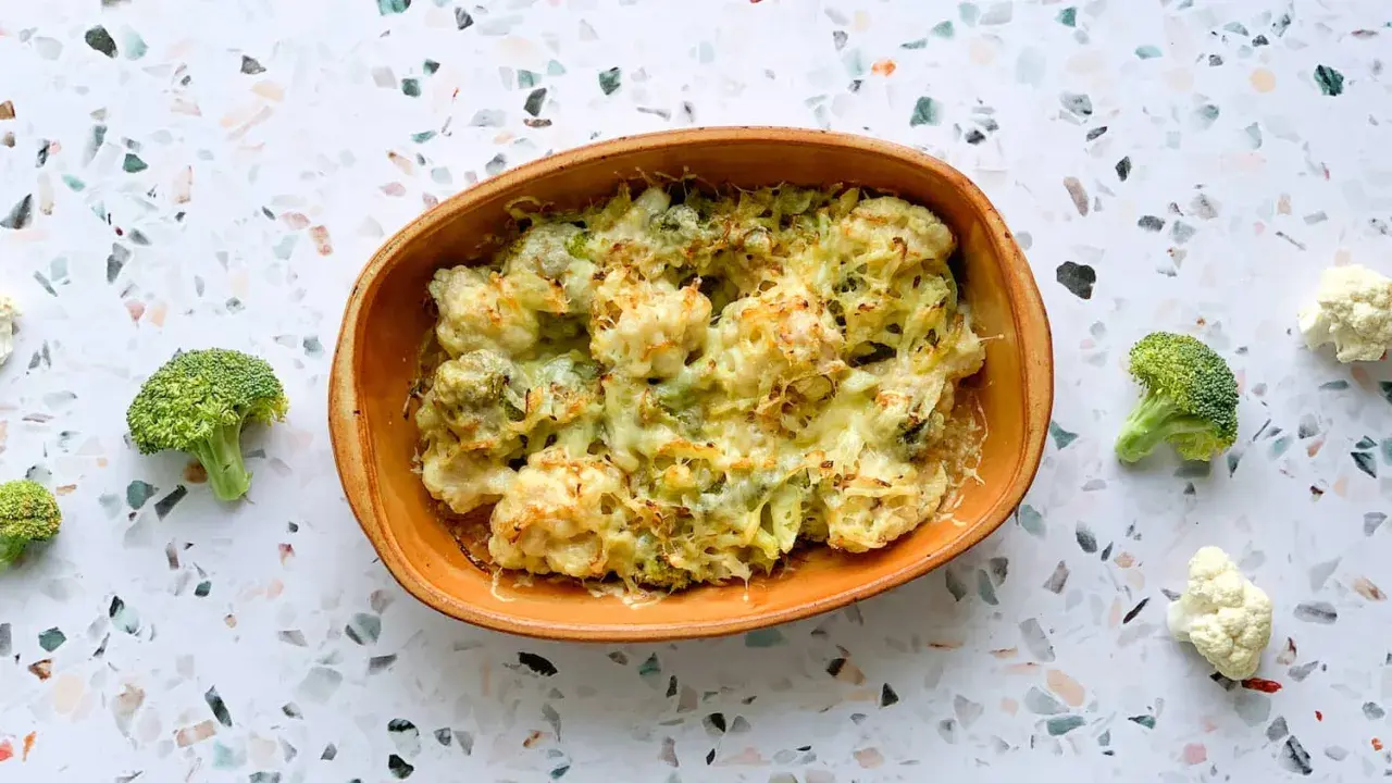 Un délicieux gratin chou-fleur brocolis, gratiné au fromage, servi dans un plat en terre cuite. Quelques fleurons frais entourent le plat.