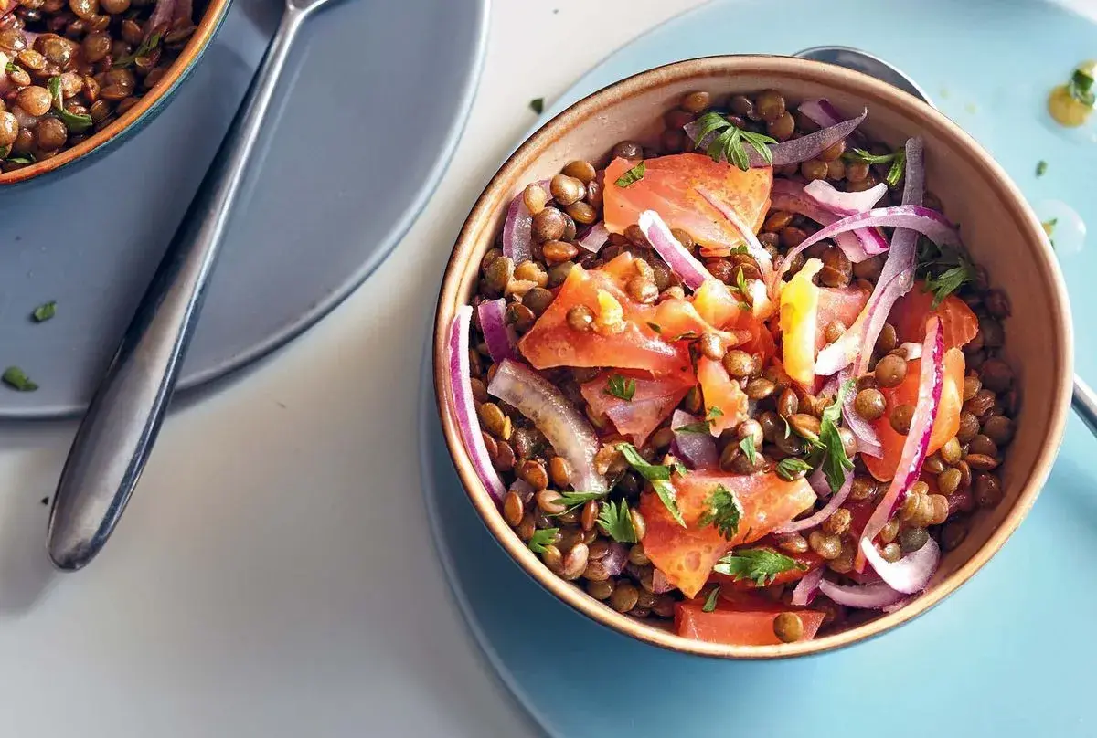 Salade de lentilles savoureuse avec du saumon fumé, des tomates et des oignons rouges, garnie de persil frais.