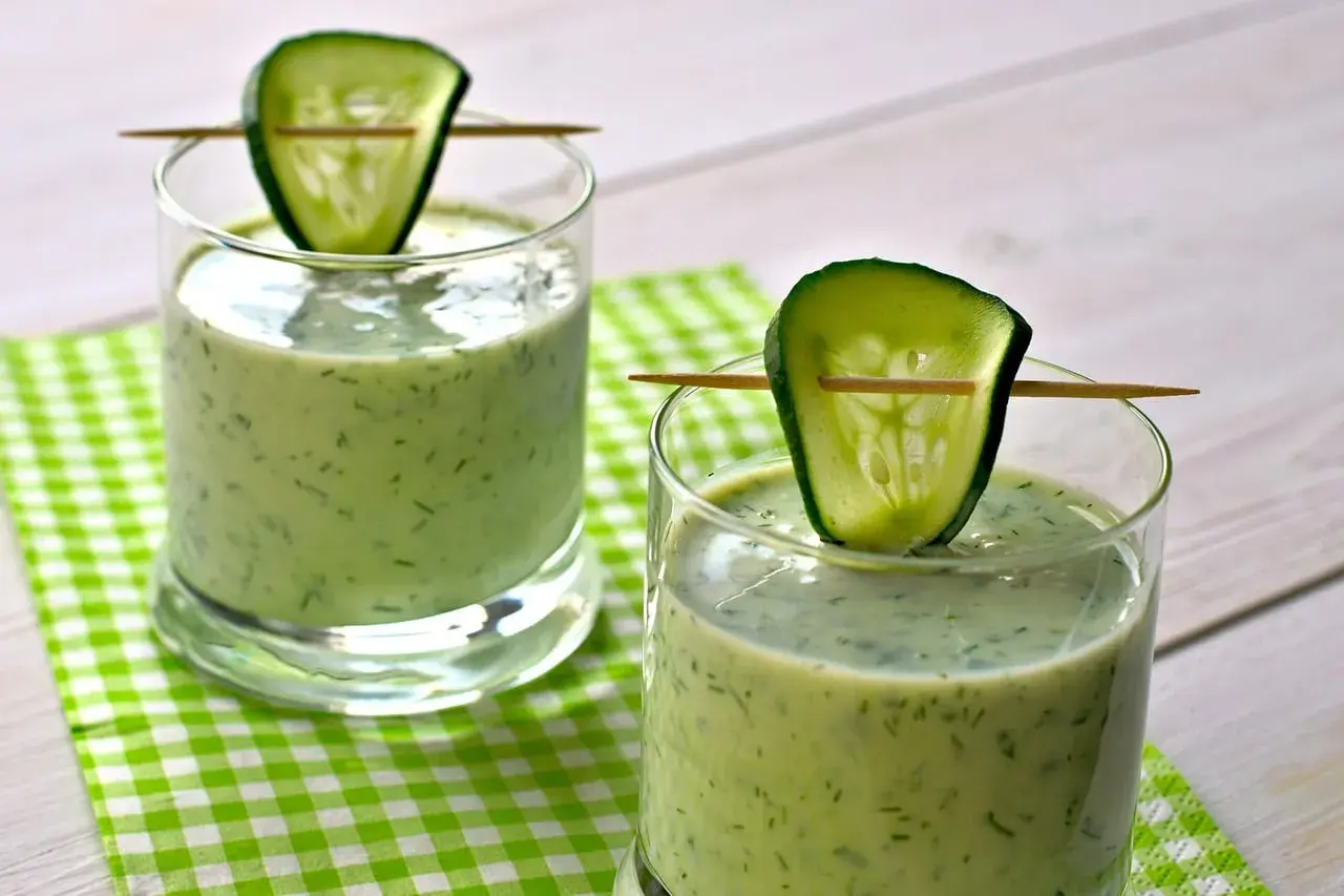 Deux verres de gaspacho concombre, décorés d'une tranche de concombre sur un cure-dent, sur une nappe à carreaux verts.