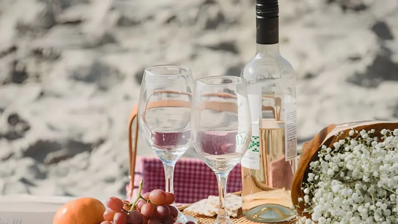 Un pique-nique sur la plage avec des verres, des raisins et une bouteille de vin. Idéal pour savoir comment choisir un vin rosé parfait pour l'occasion.