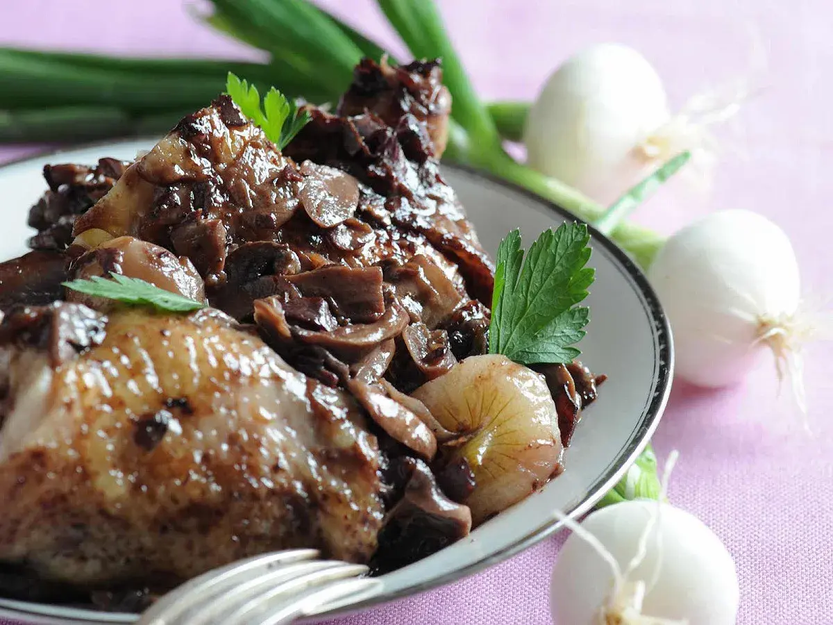 Coq au vin savoureux, garni de champignons et d'oignons. Parfait pour savoir que boire avec un coq au vin.