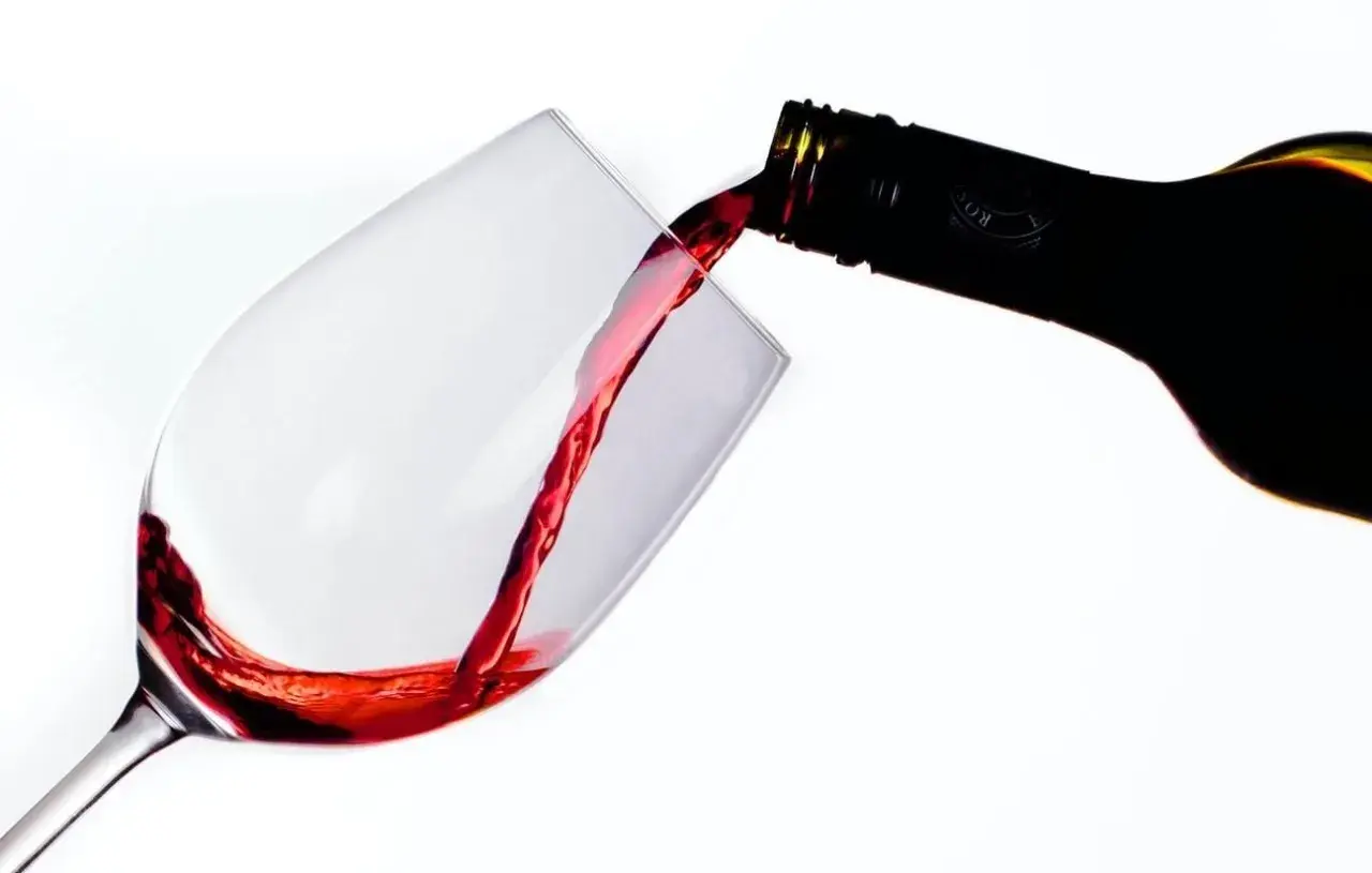 Le vin rouge, fruit d'une macération soignée, coule d'une bouteille dans un verre.
